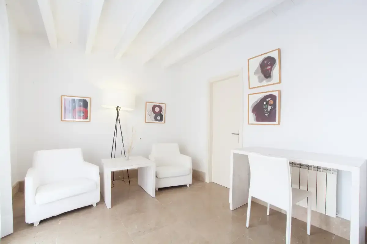 Una luminosa zona de estar tiene dos sillones, cuadros enmarcados y un escritorio.