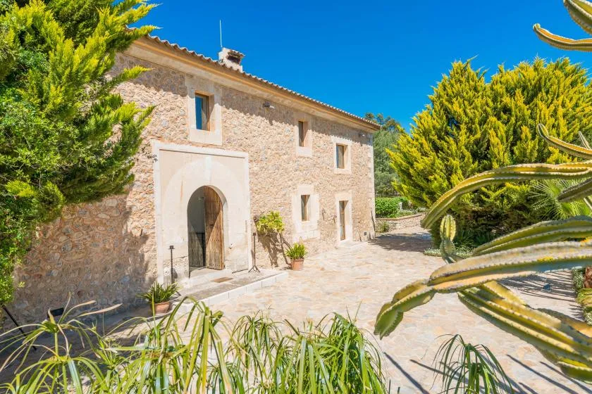 Una casa de piedra se encuentra junto a un patio pavimentado con plantas.