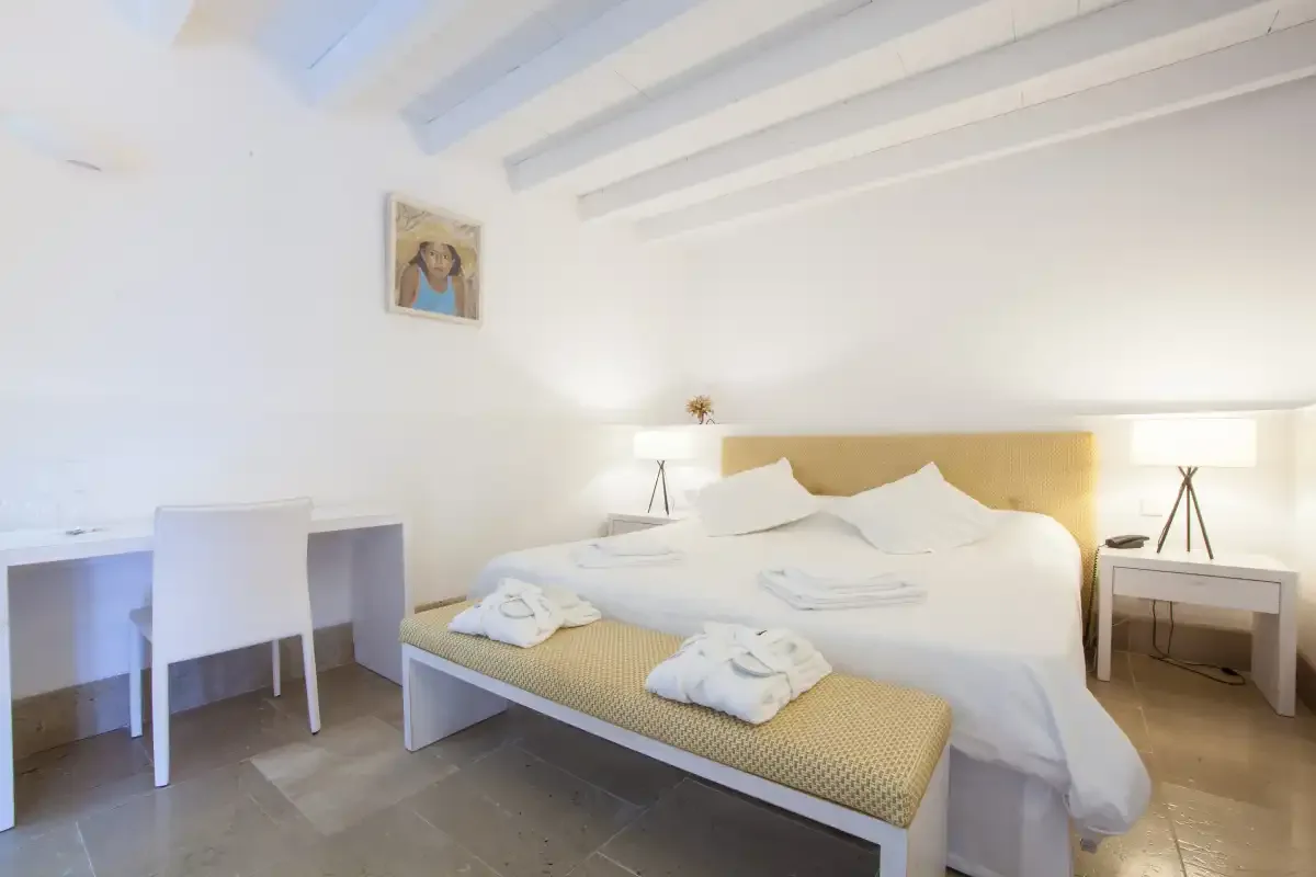 Un dormitorio luminoso con una cama bien arreglada y un escritorio junto a la pared.