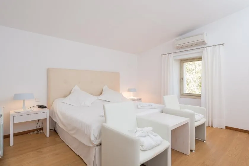Un dormitorio luminoso con una cama y asientos blancos junto a una ventana.