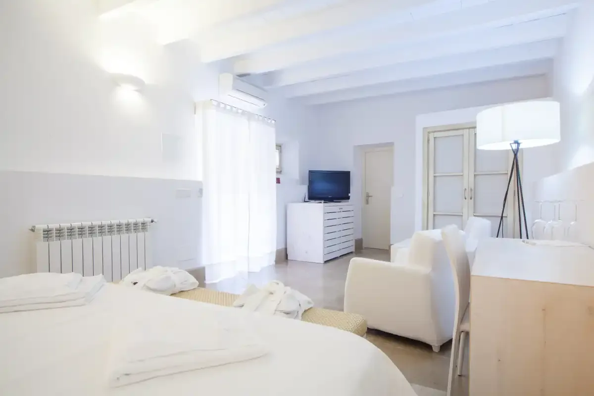 Un dormitorio luminoso con una cama, un televisor sobre una cómoda y una zona de estar.