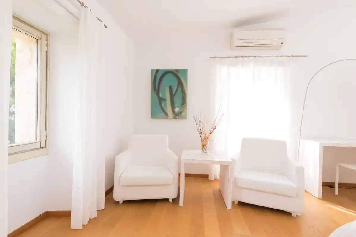 Una luminosa zona de estar con dos asientos y una mesita junto a una ventana.