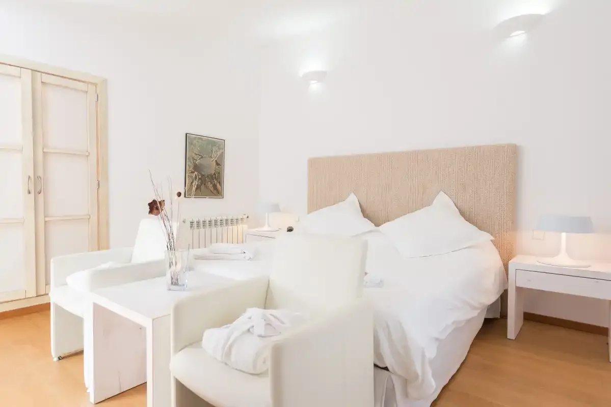 Un dormitorio luminoso con una cama, asientos blancos y un escritorio.