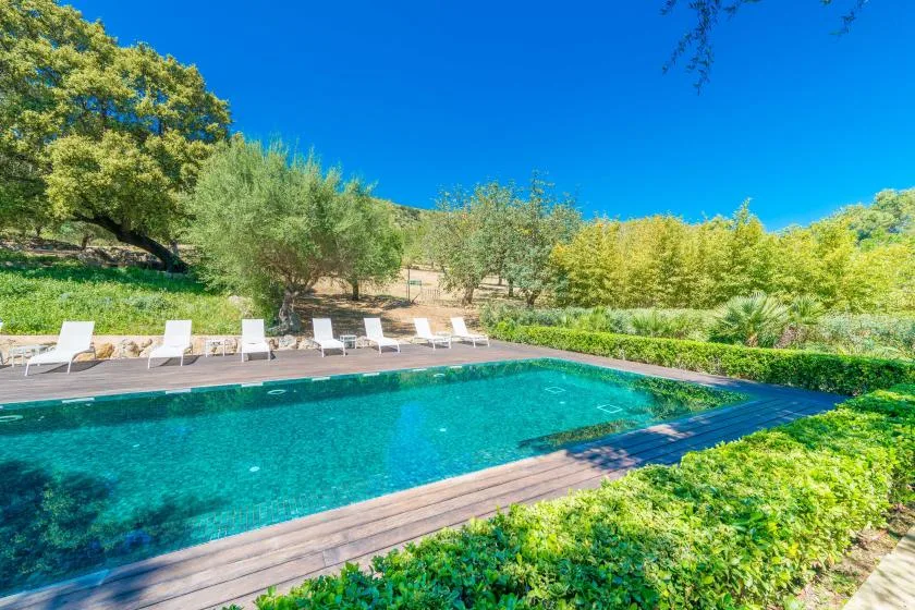 Una piscina al aire libre rodeada de una tarima de madera y asientos reclinables.