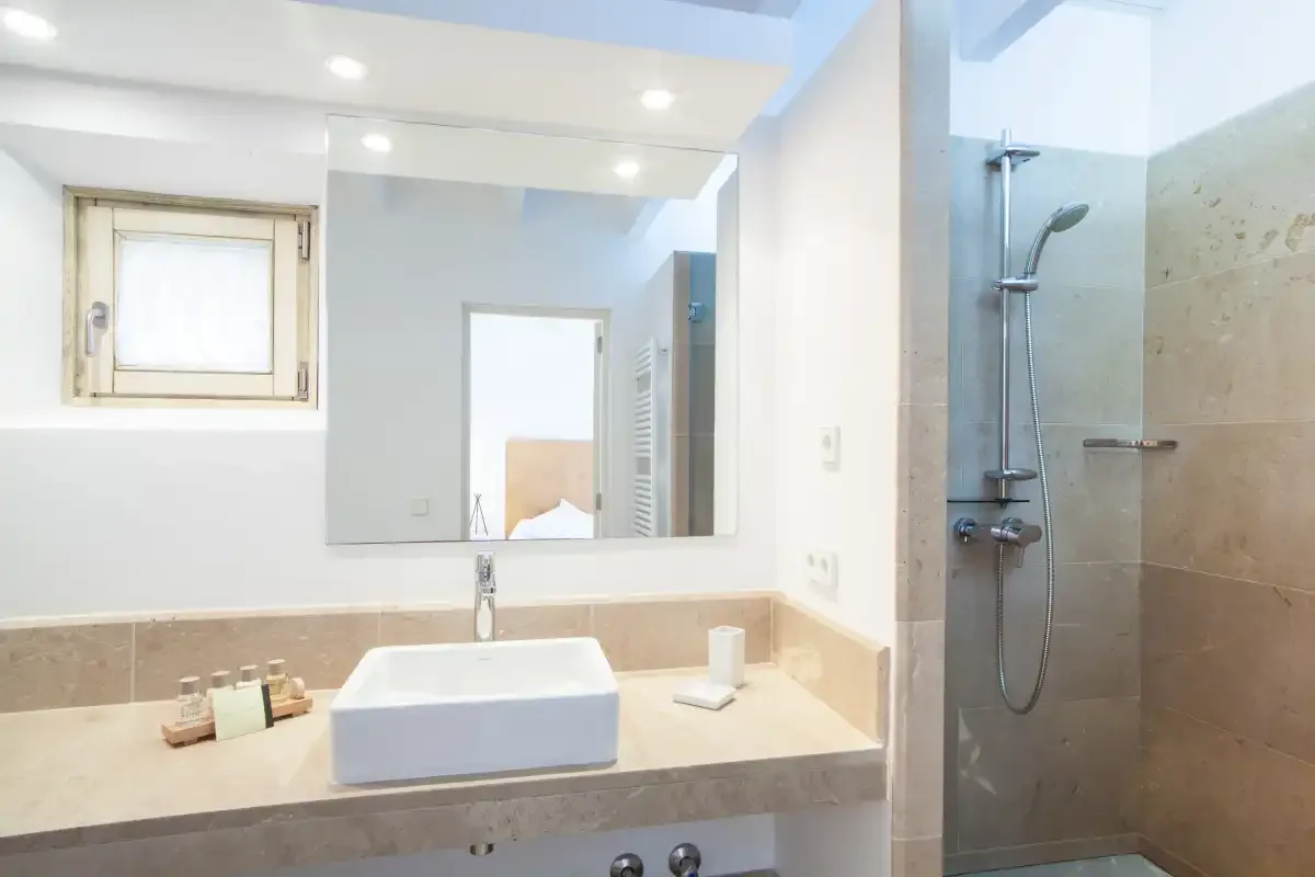 Un baño luminoso con lavabo, espejo amplio y ducha.