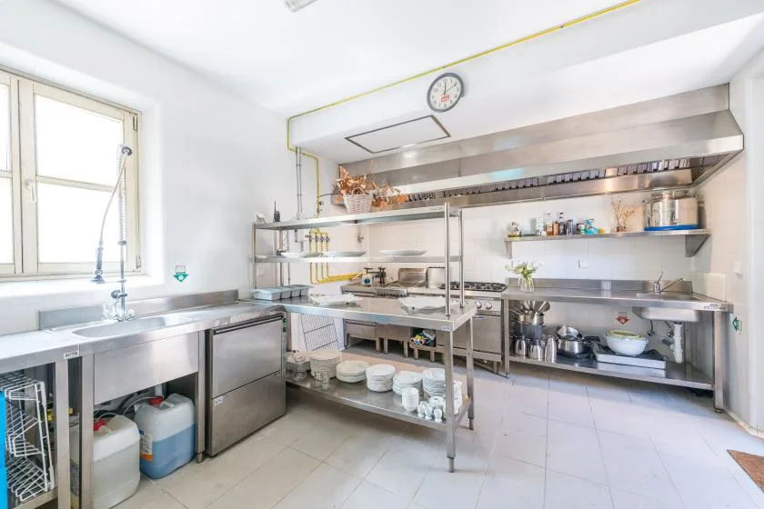 Una cocina comercial con encimeras de acero inoxidable y una gran campana extractora.