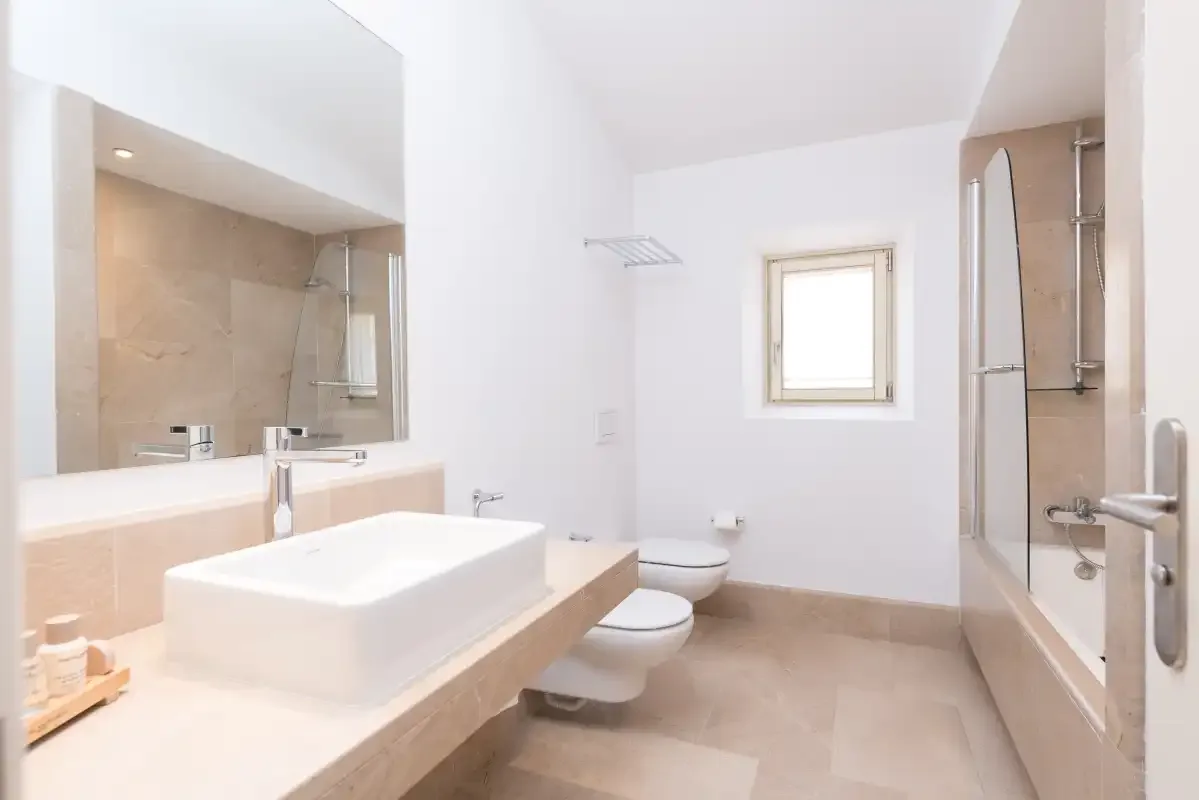 Un baño luminoso con lavabo, inodoro suspendido y ducha de vidrio.