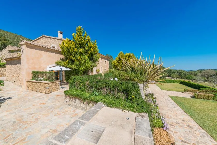 Un sendero de piedra conduce hacia una casa, con arbustos y césped abierto.