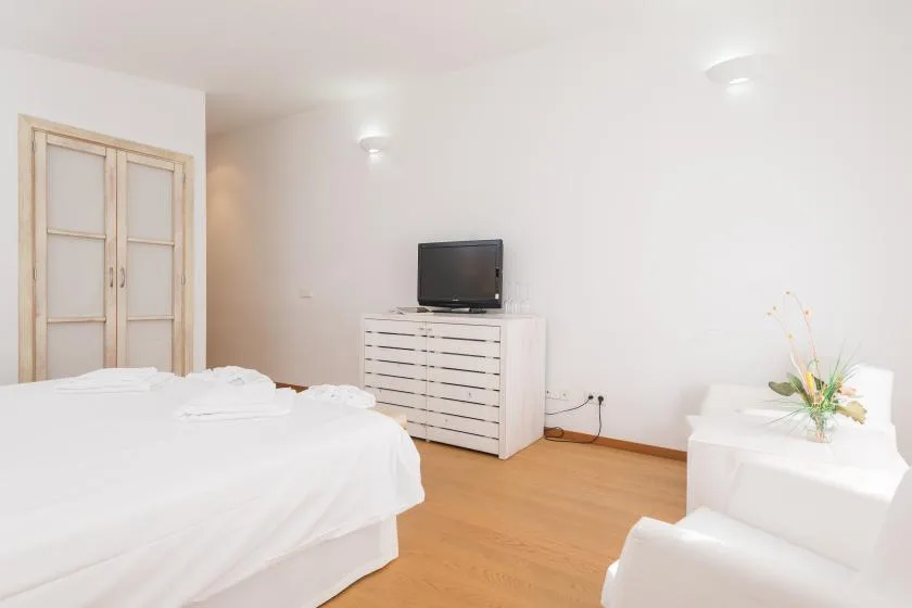 Un dormitorio luminoso con una cama, un televisor sobre una cómoda y una mesita.