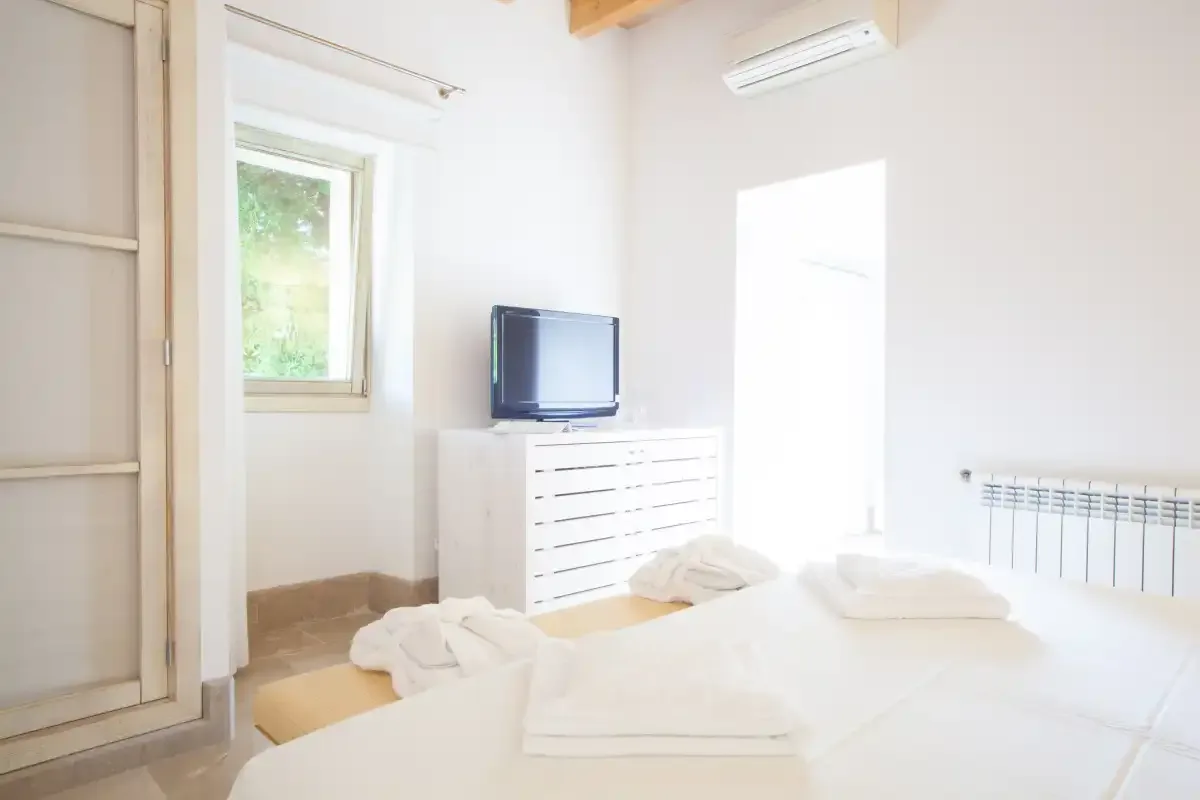 Un dormitorio luminoso con ropa de cama blanca, una cómoda y un televisor.