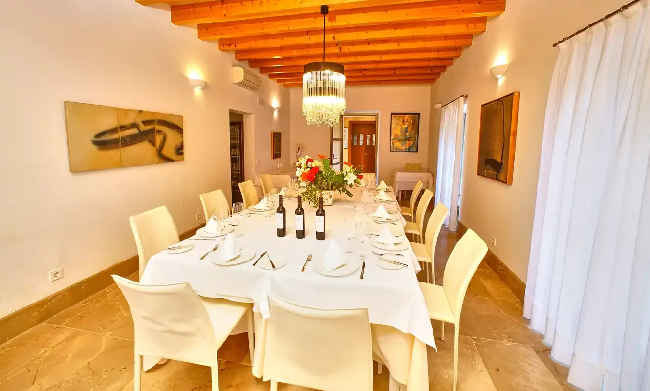 Un comedor con una mesa larga preparada con mantelería blanca y cubiertos.