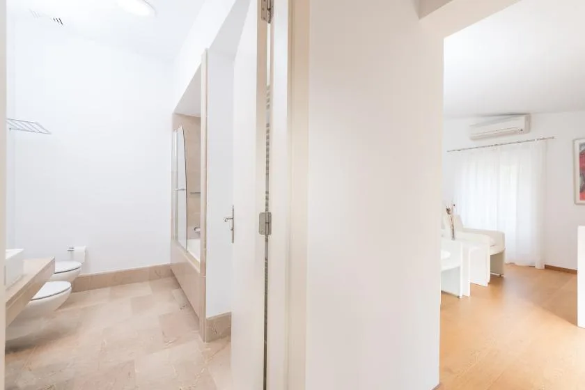 Un pasillo luminoso da a un baño y a una habitación con escritorio.