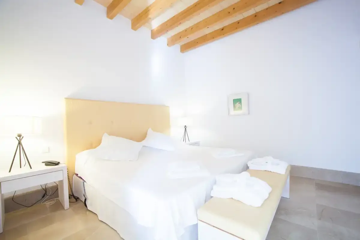 Un dormitorio luminoso con una cama arreglada y vigas de madera a la vista en el techo.