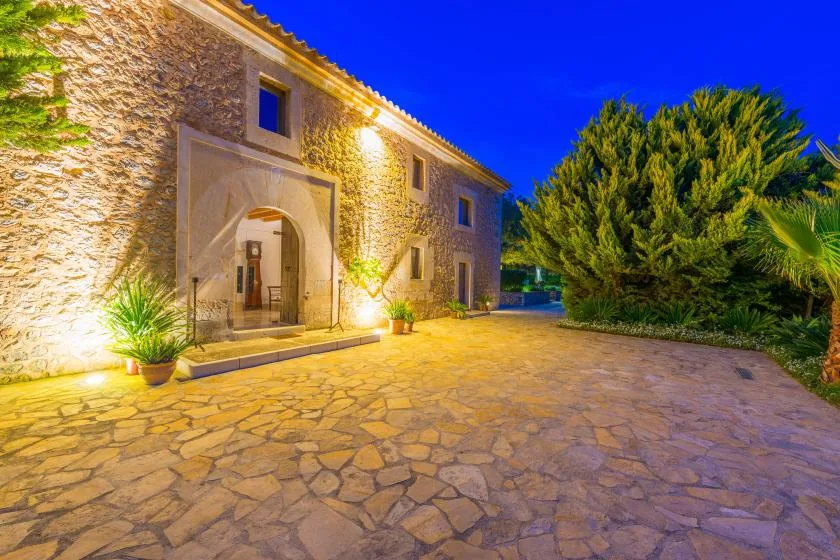 La entrada de un edificio de piedra da a un patio pavimentado al anochecer.