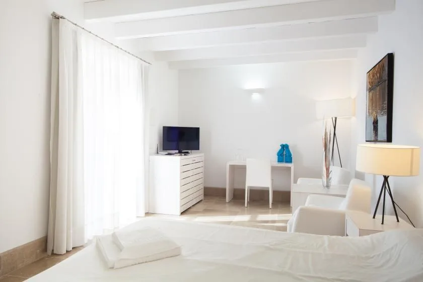 Un dormitorio luminoso con una cama, un televisor y un pequeño escritorio.