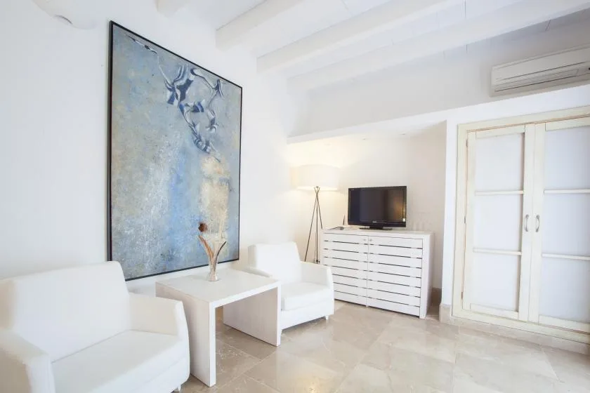 Una sala luminosa con asientos blancos, un televisor y una obra enmarcada.