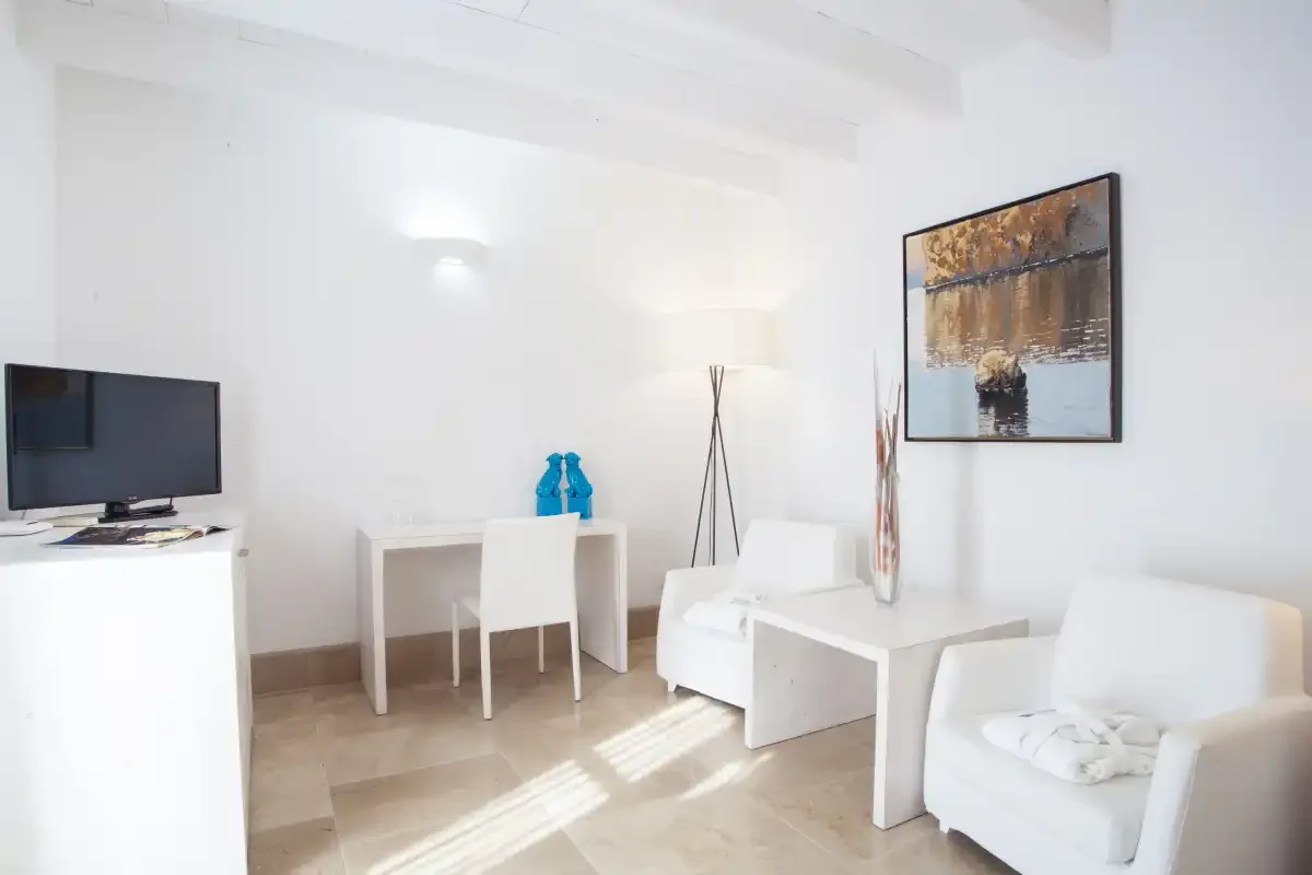 Una luminosa sala de estar blanca con asientos, un televisor y arte enmarcado en la pared.