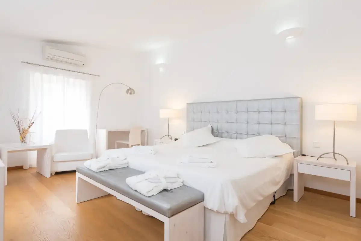 Un dormitorio luminoso con una cama grande, cabecero acolchado y mesillas de noche.