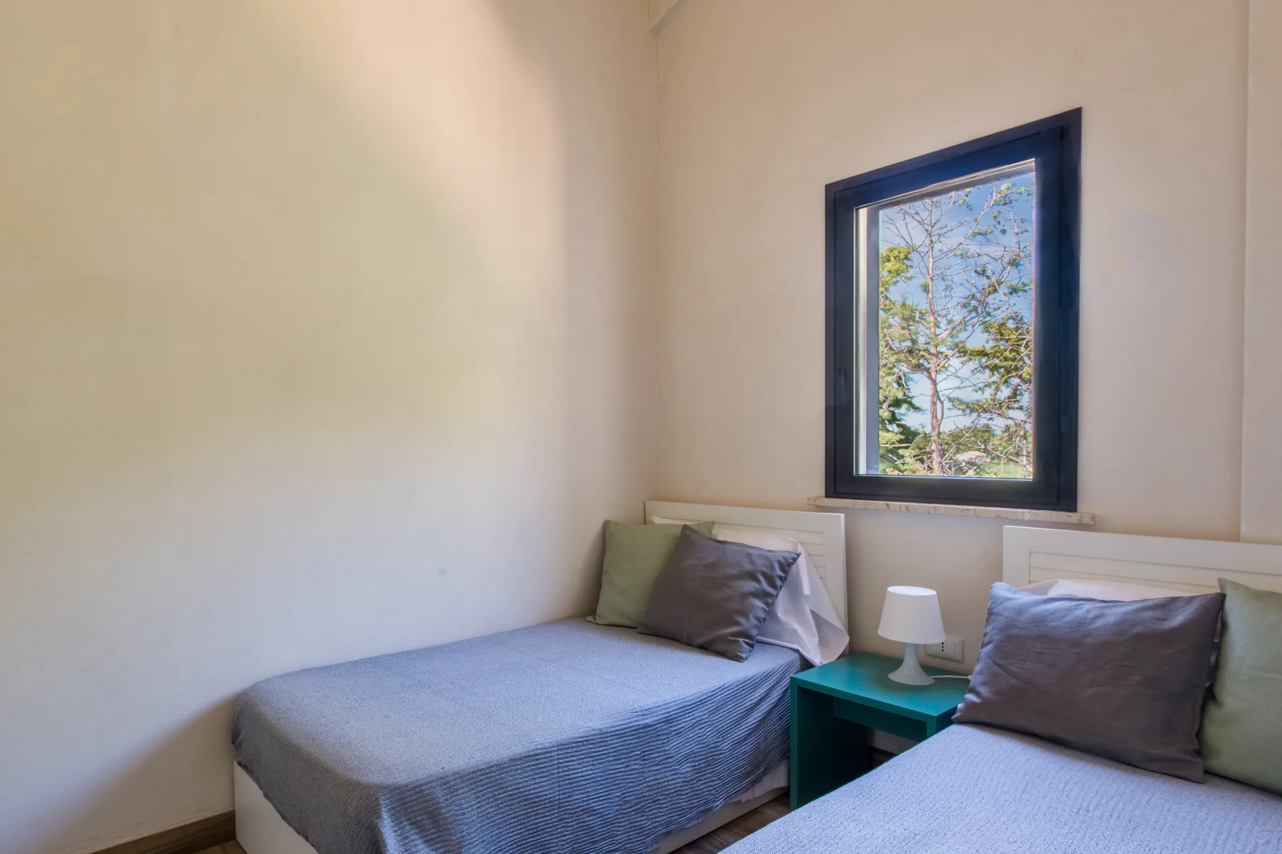 A bedroom with two beds beside a window overlooking trees.