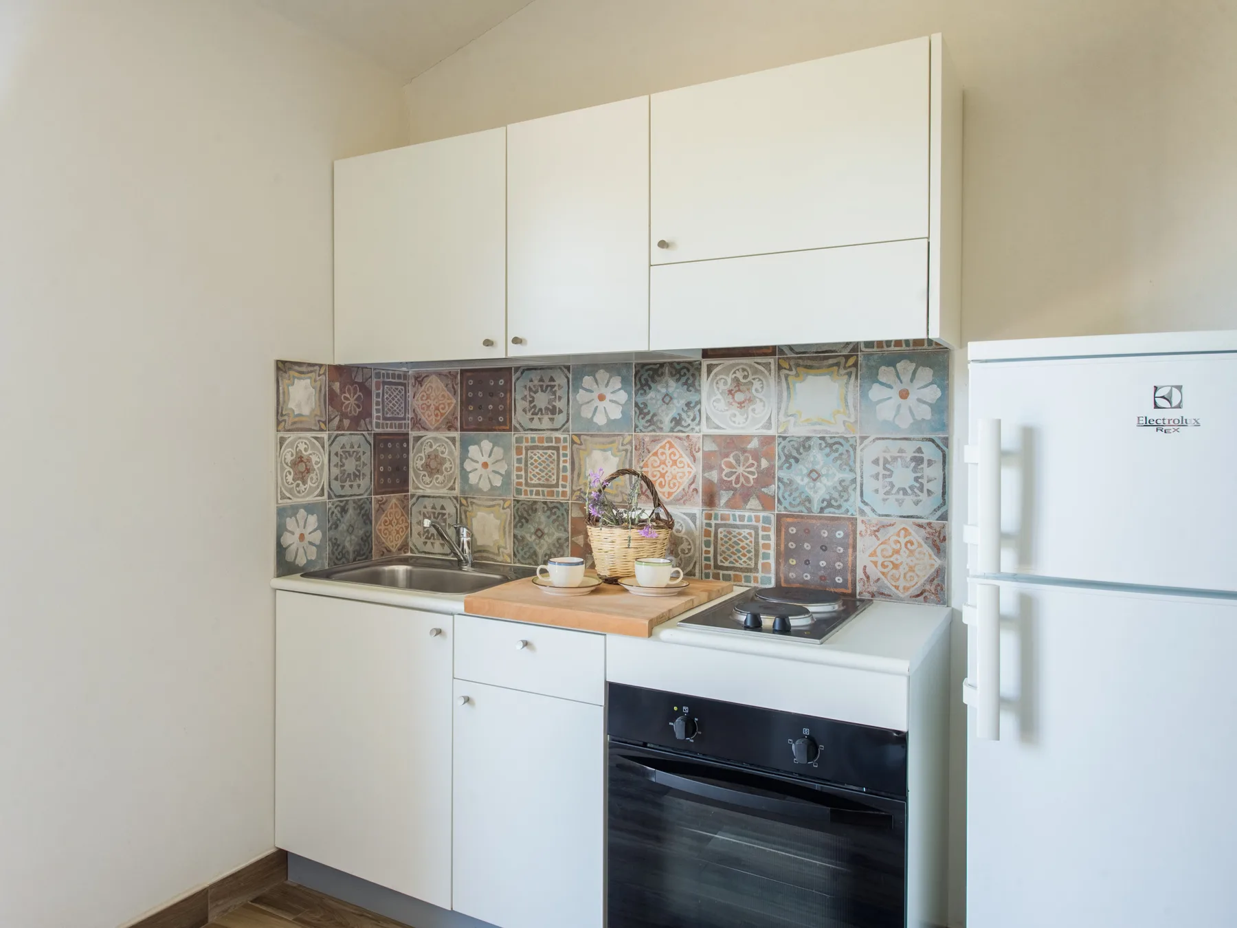 A compact kitchen with white cabinets, a tiled backsplash, and a refrigerator.