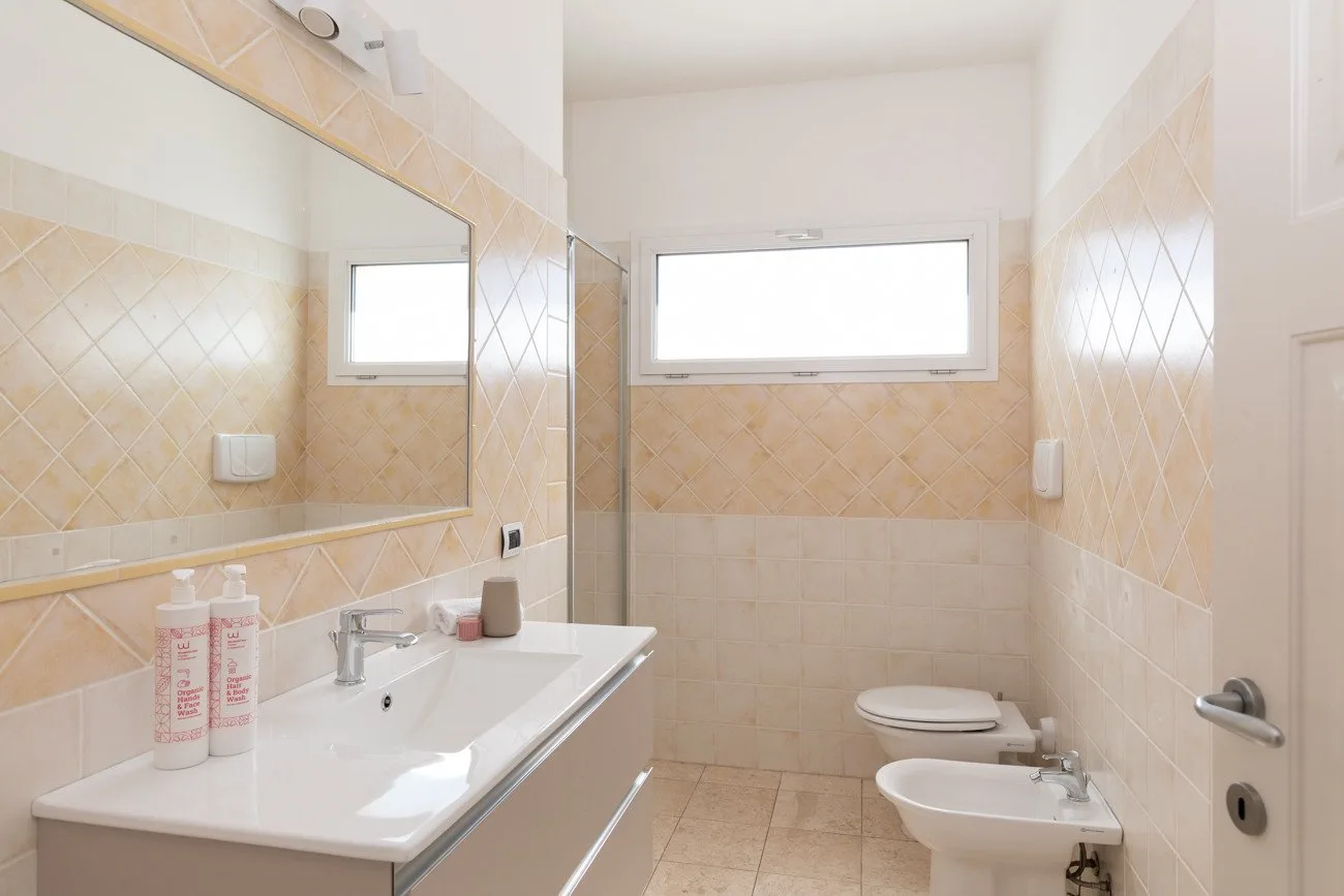 Un baño luminoso con azulejos, lavabo, espejo, inodoro y bidé.