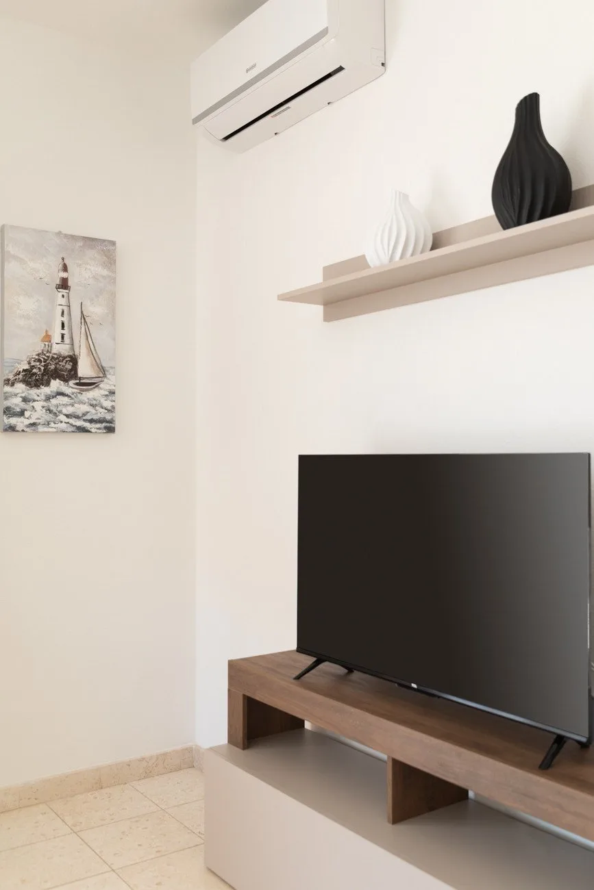 Un rincón luminoso de sala de estar con un televisor sobre una consola de madera y arte en la pared.