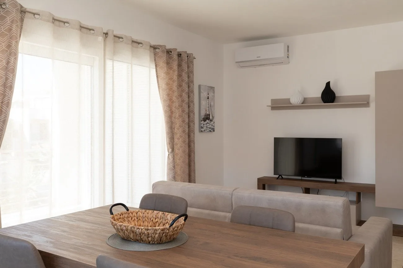 Una sala luminosa con televisión, asientos y una mesa de comedor.