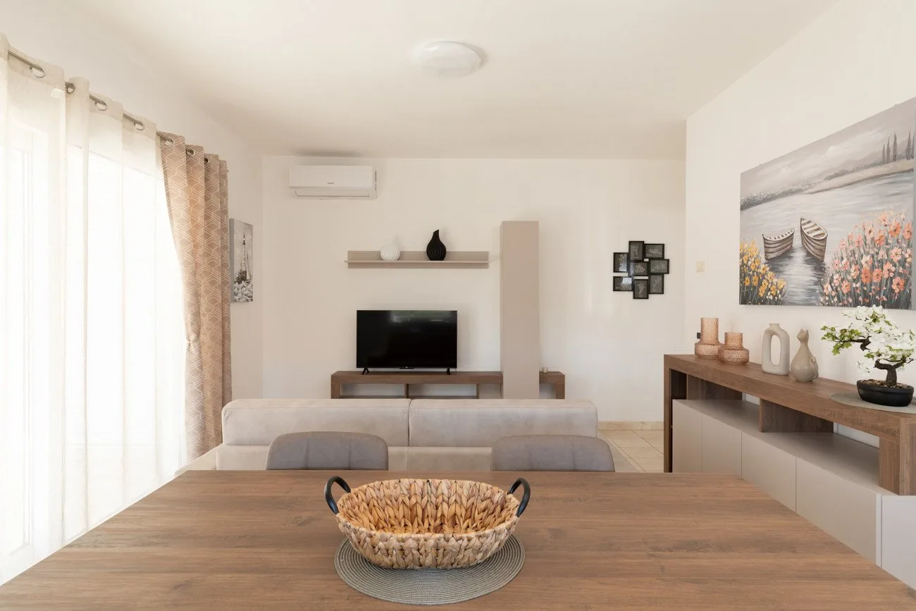 Un salón-comedor luminoso con un televisor y una mesa de madera.