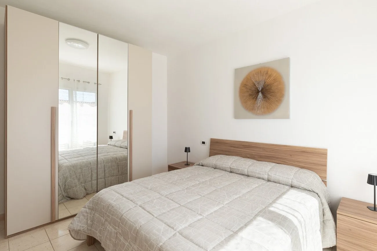 Un dormitorio luminoso con una cama tendida y un armario con espejo.