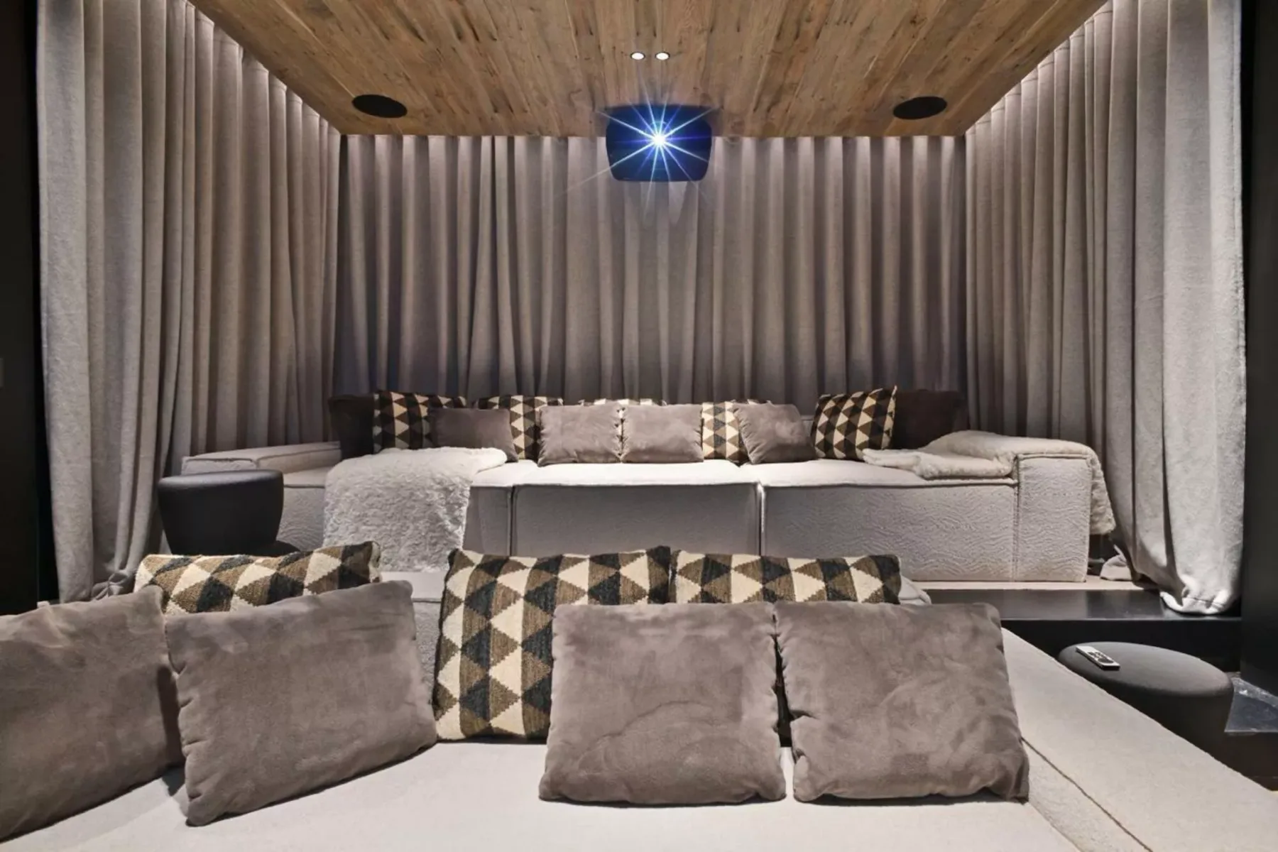 Una zona de estar con cojines, bajo un techo revestido de madera y cortinas.