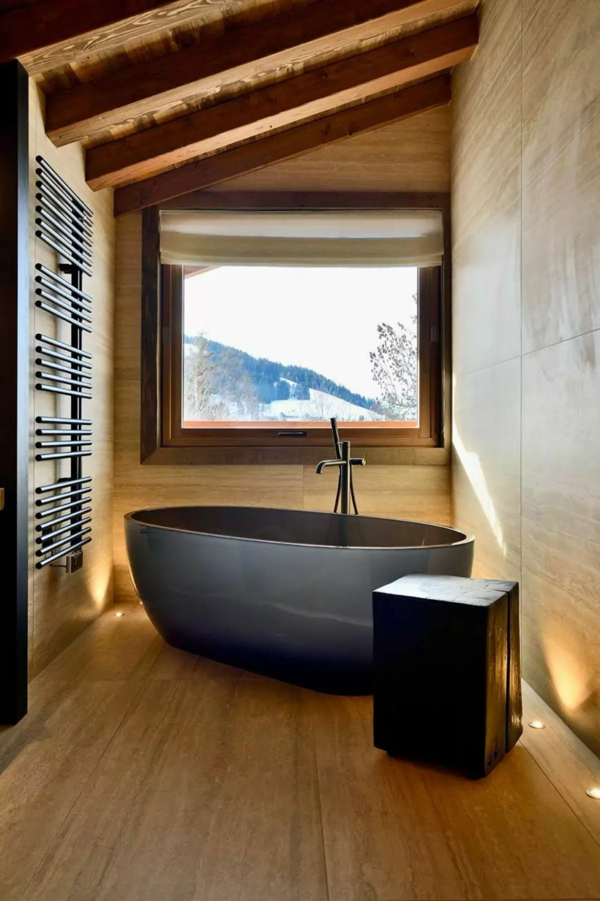 Una bañera exenta está bajo una ventana en un baño con techo inclinado de madera.