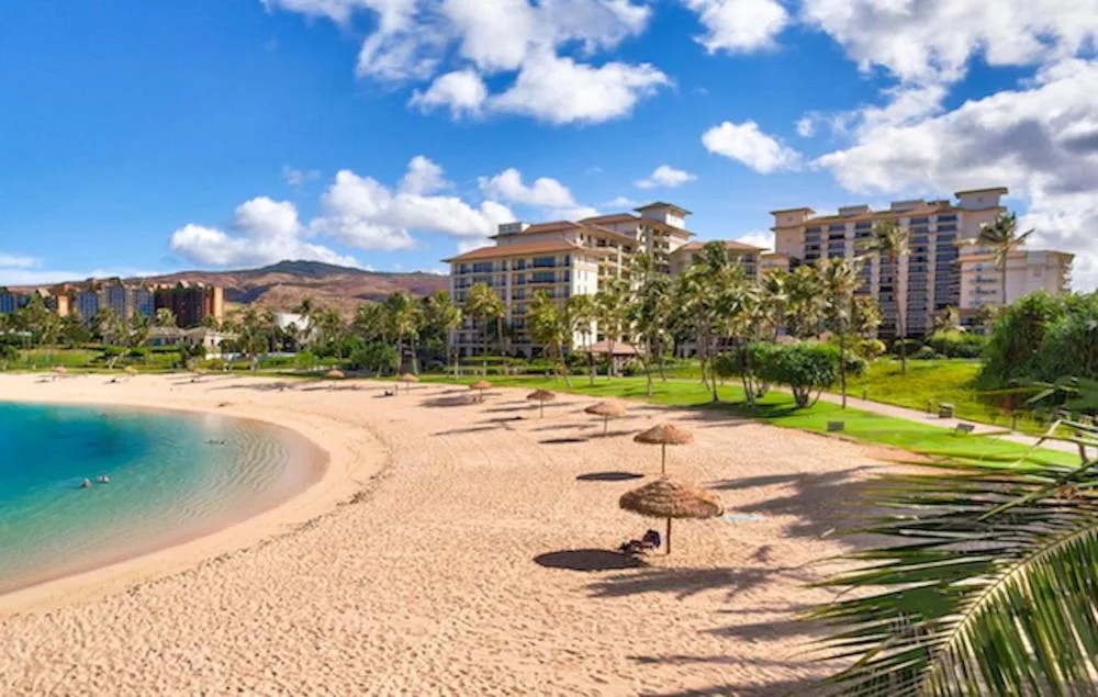 Una playa de arena se curva junto al agua turquesa, con edificios y palmeras detrás.