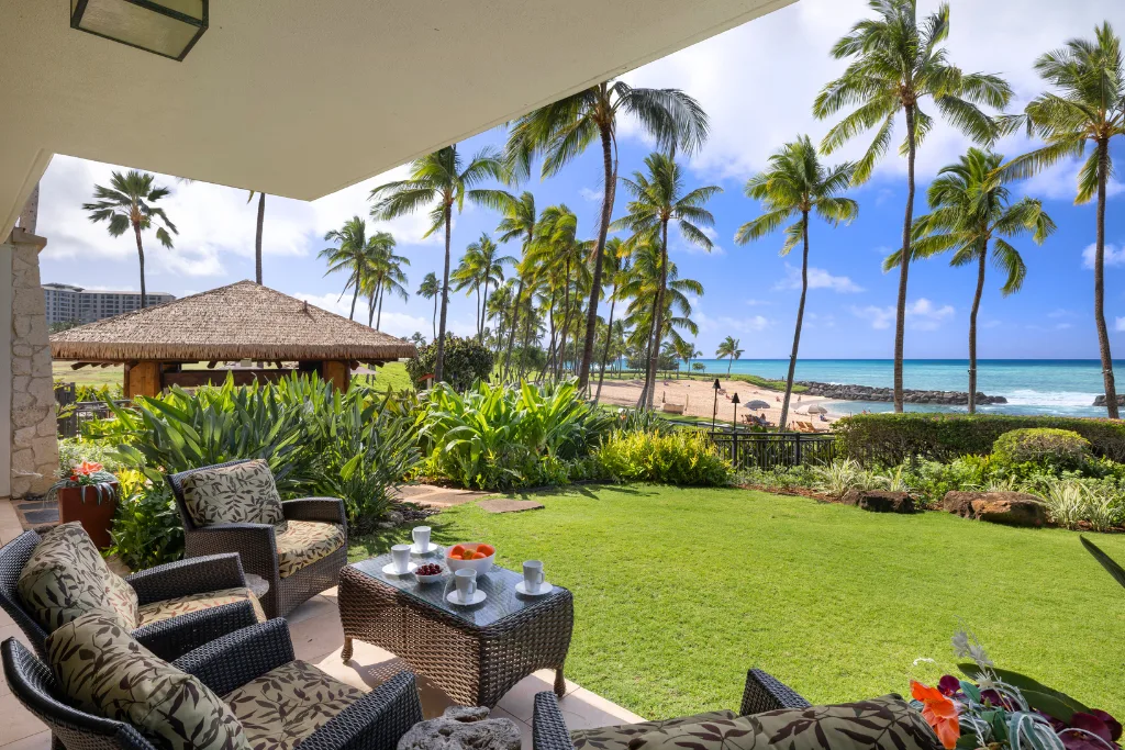 Un jardín con asientos al aire libre da a una playa bordeada de palmeras y al océano.