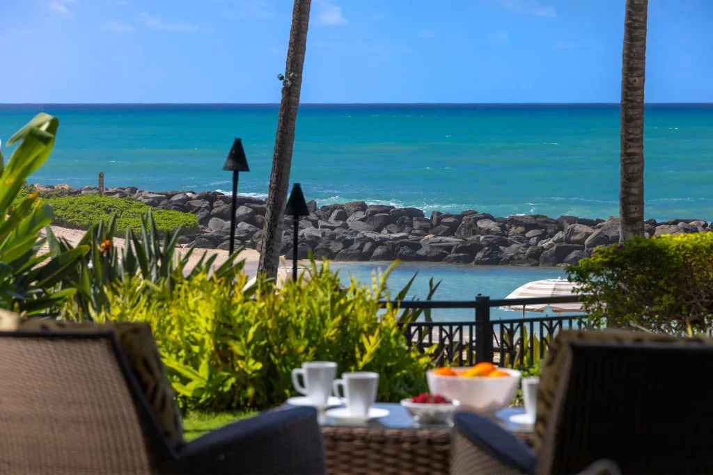 Un patio junto al mar da a aguas turquesas, con asientos al aire libre y una mesa baja en primer plano.