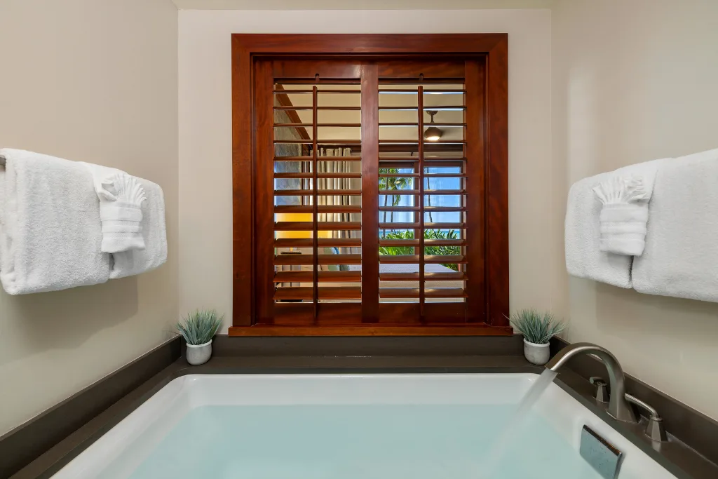 Un baño con una bañera bajo una ventana con persianas de madera.