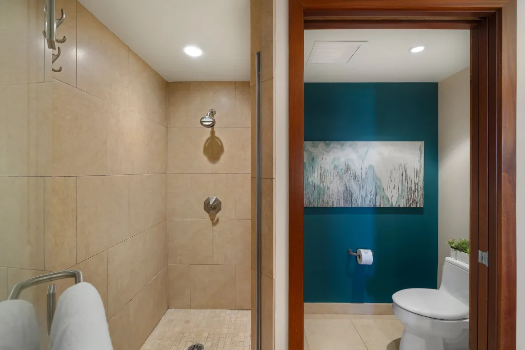 Un baño con azulejos, una ducha junto al inodoro y una pared de acento turquesa.