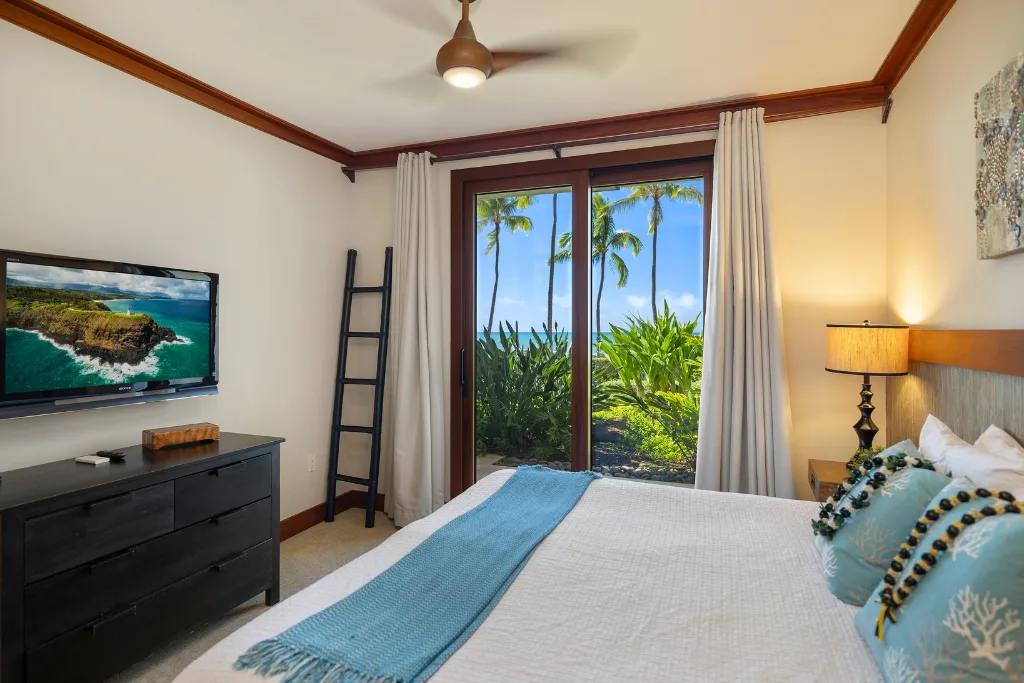 Un dormitorio con cama, televisor y una ventana con vista a vegetación tropical.