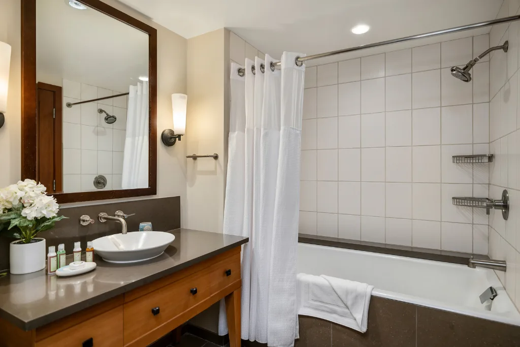 Un baño con lavabo, espejo y bañera detrás de una cortina de ducha.