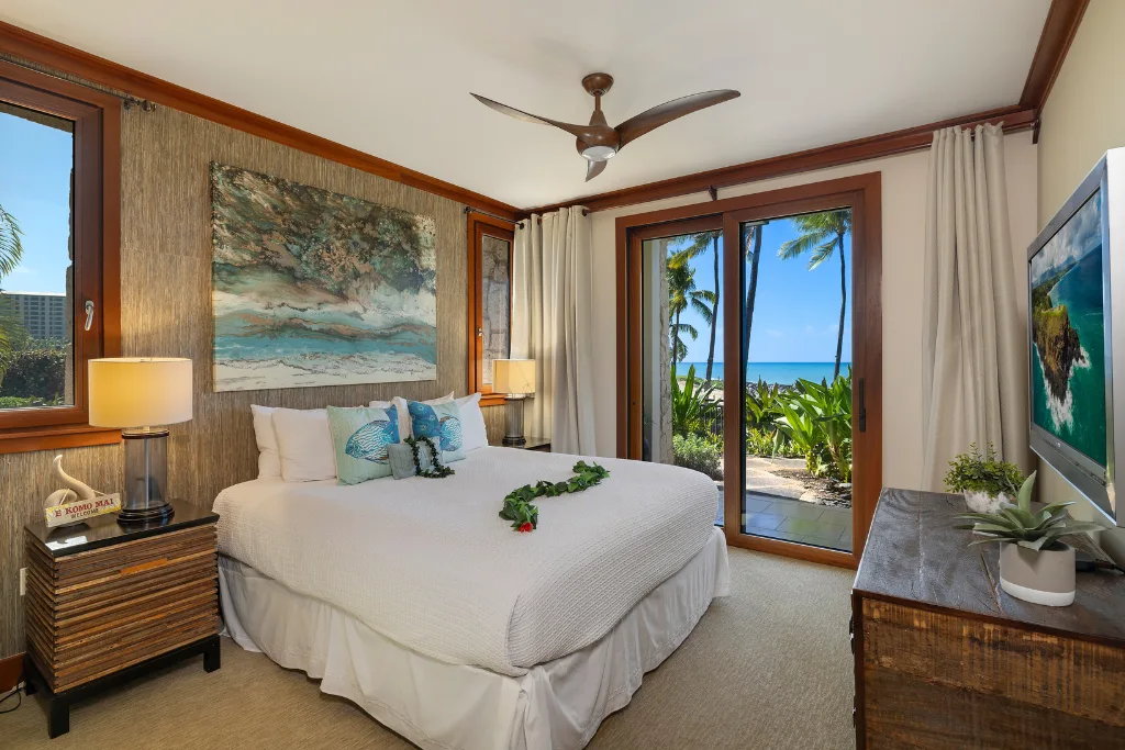 Un dormitorio con una cama grande, una obra enmarcada y puertas de vidrio con vistas tropicales.