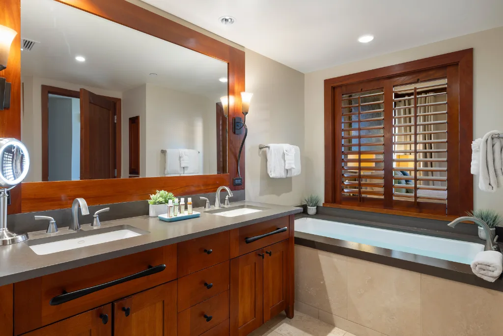 Un tocador de baño con un espejo amplio está junto a una ventana con persianas de madera.