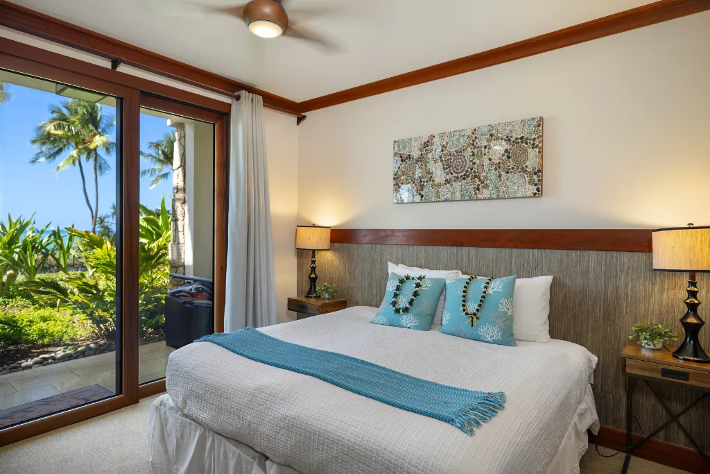 Un dormitorio con una cama vestida de blanco y detalles azules junto a una puerta de vidrio.