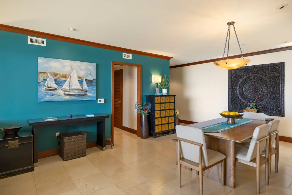 Un comedor con mesa y sillas está junto a una pared turquesa con una obra de arte.