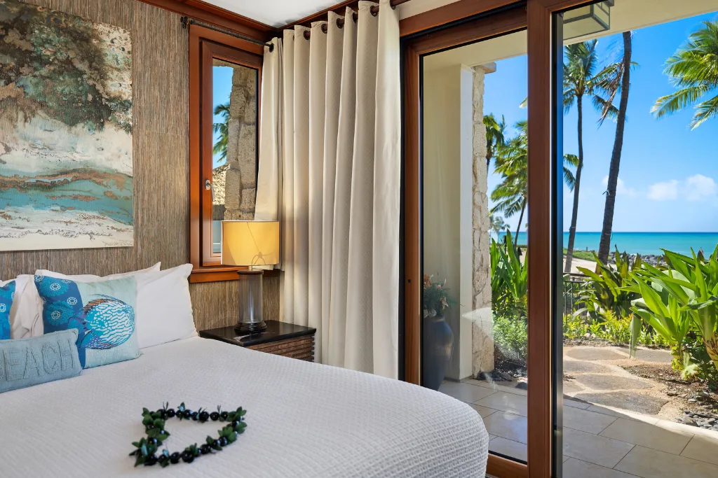 Un dormitorio con una cama junto a una puerta de vidrio con vistas tropicales.