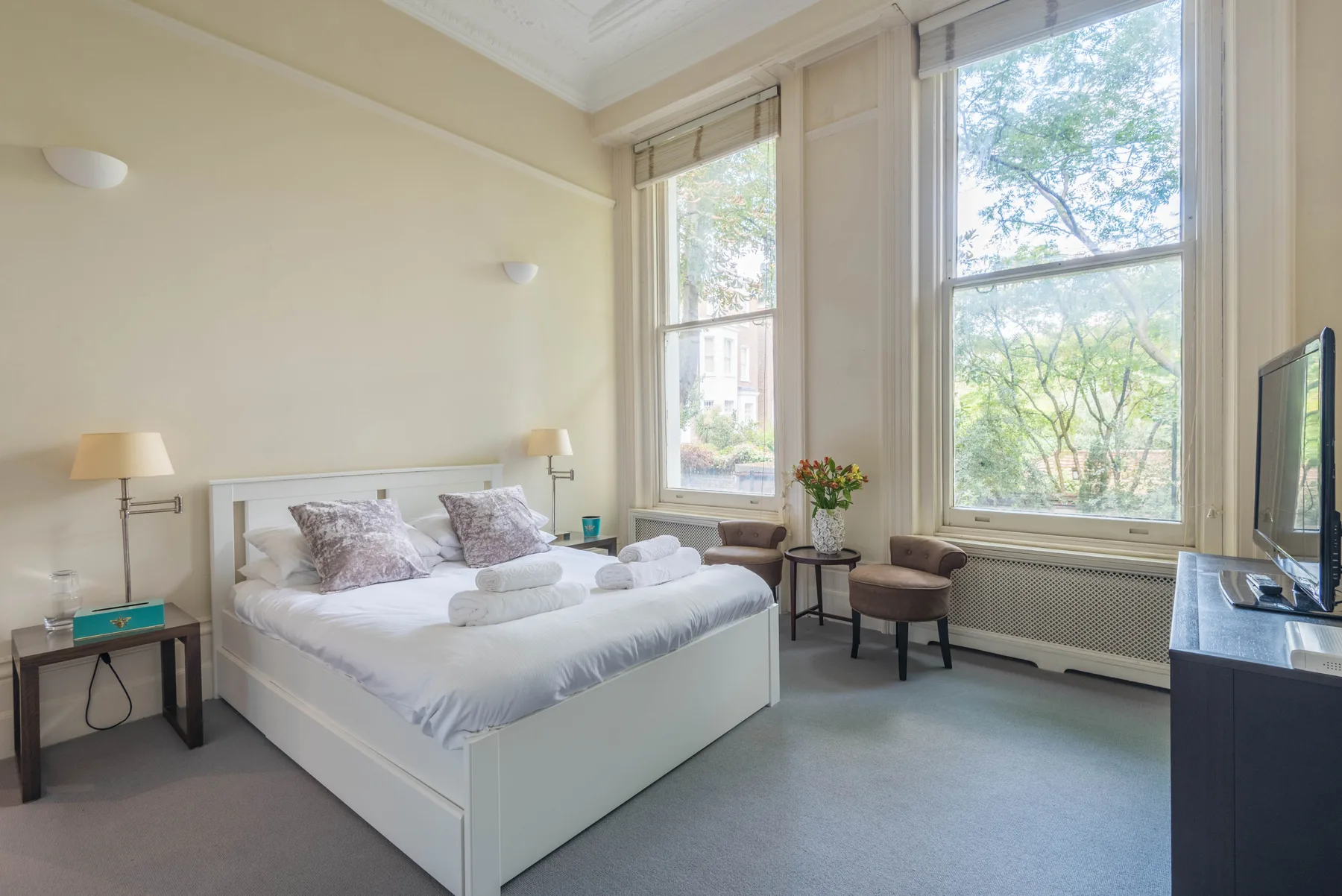 Un dormitorio luminoso con una cama bien hecha junto a ventanas altas.