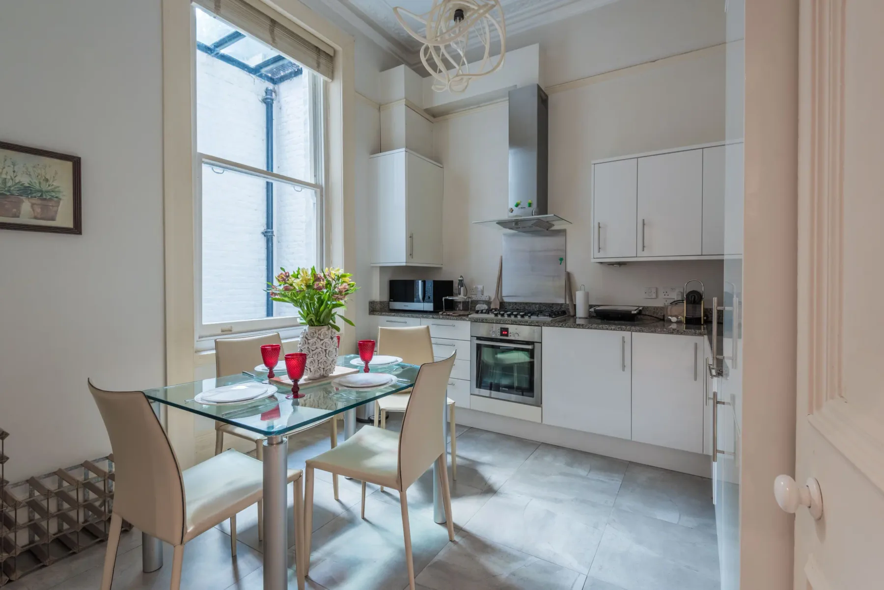 Una cocina luminosa con una mesa de comedor de vidrio y armarios blancos.