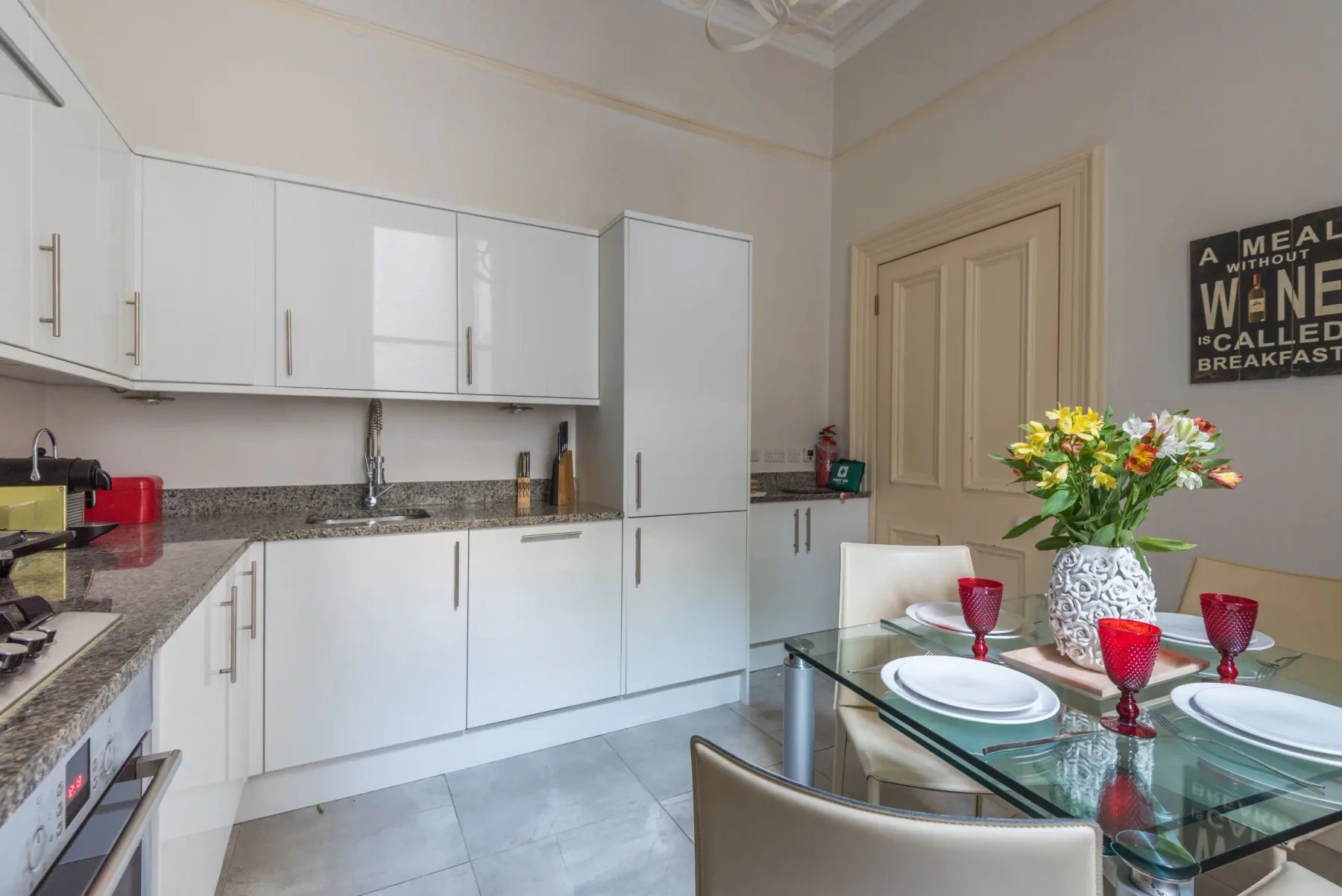 Una cocina luminosa con gabinetes blancos y una mesa de comedor de vidrio.