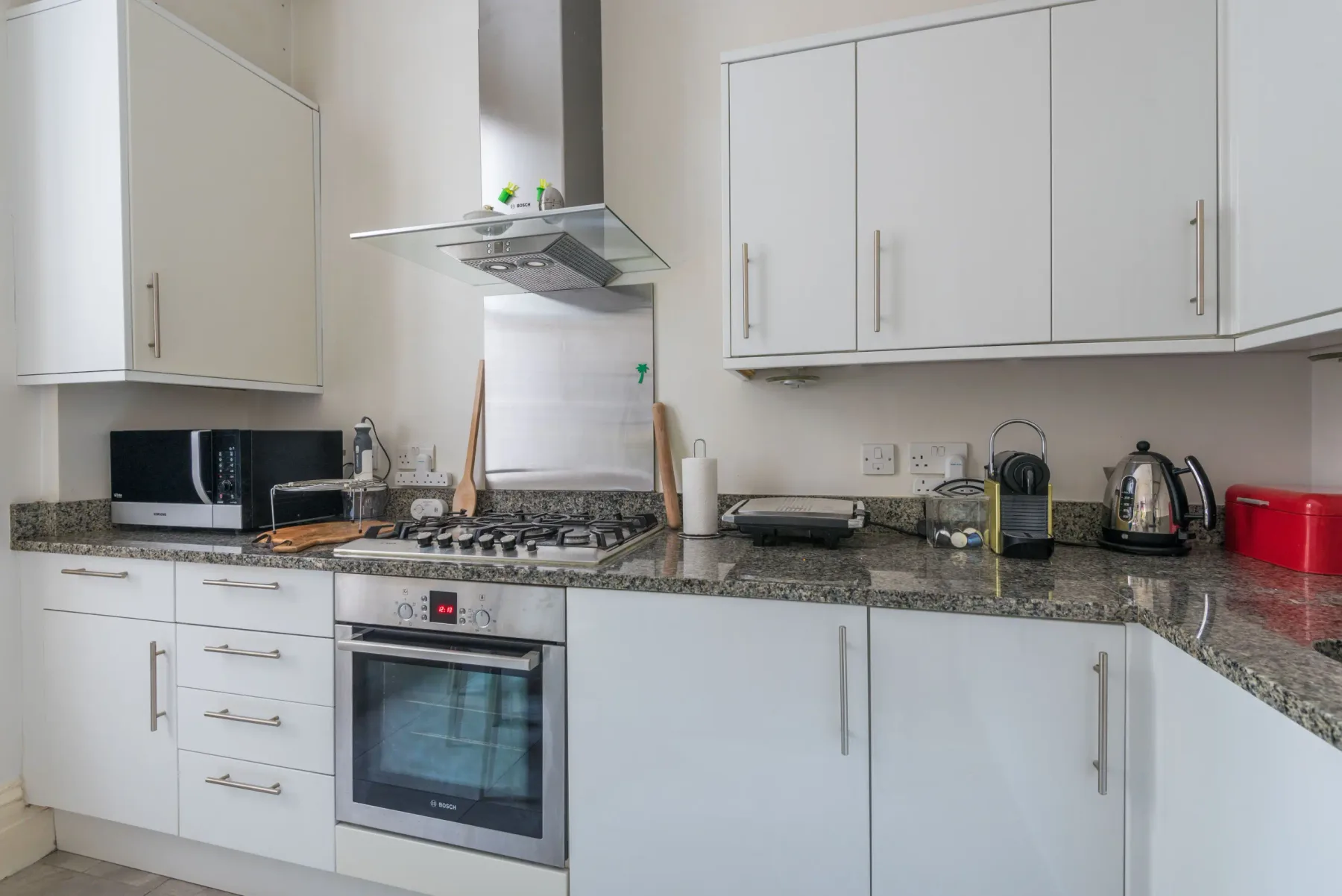 Una cocina luminosa con gabinetes blancos, una estufa y electrodomésticos sobre la encimera.