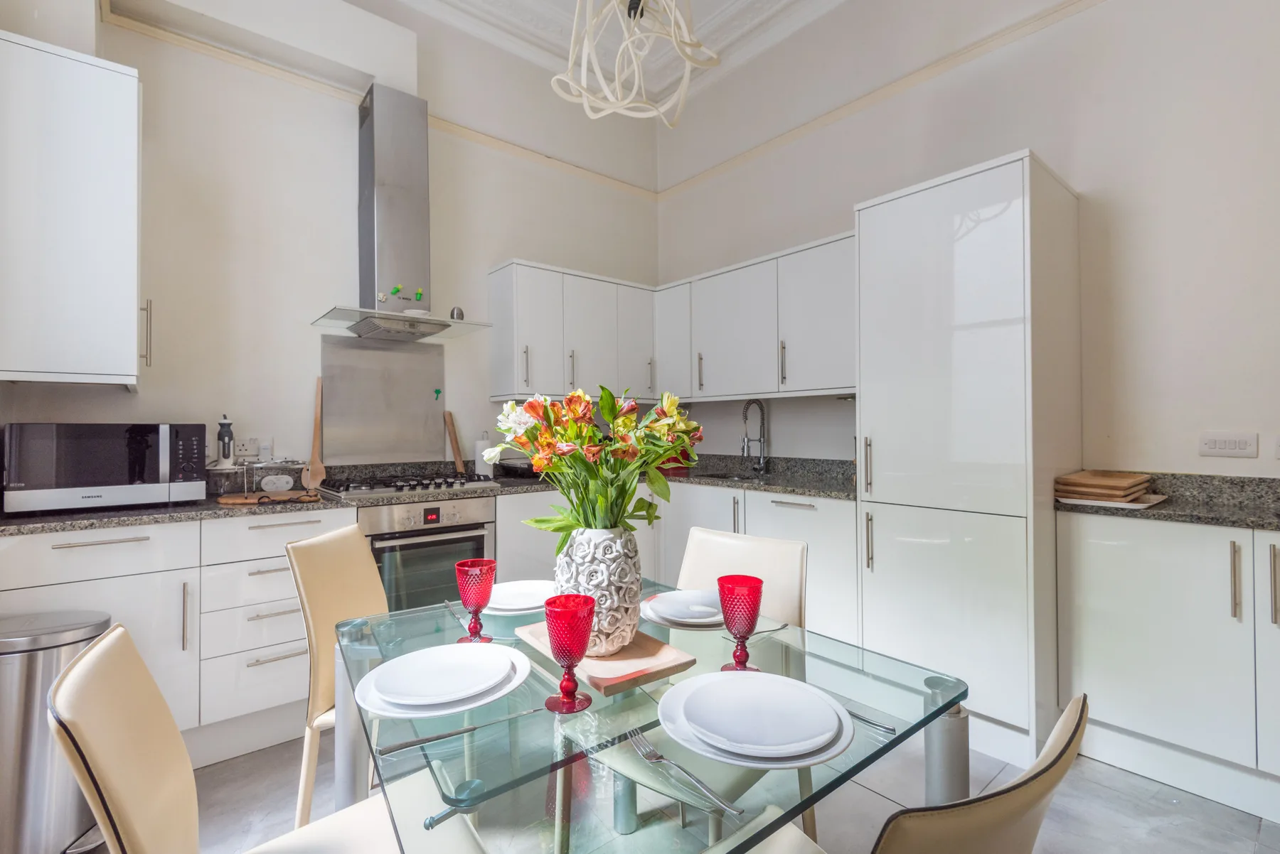 Una cocina luminosa con gabinetes blancos y una mesa de vidrio.