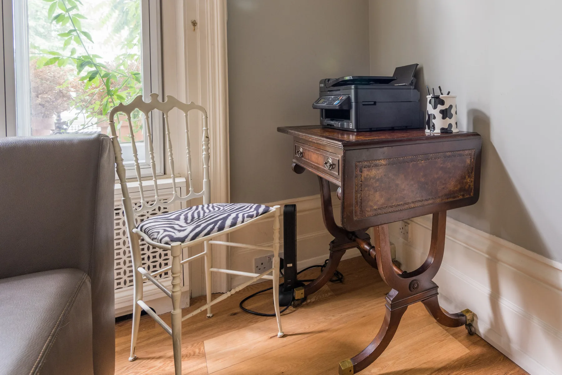 Una luminosa zona de estar con una silla junto a un escritorio de madera y una impresora.