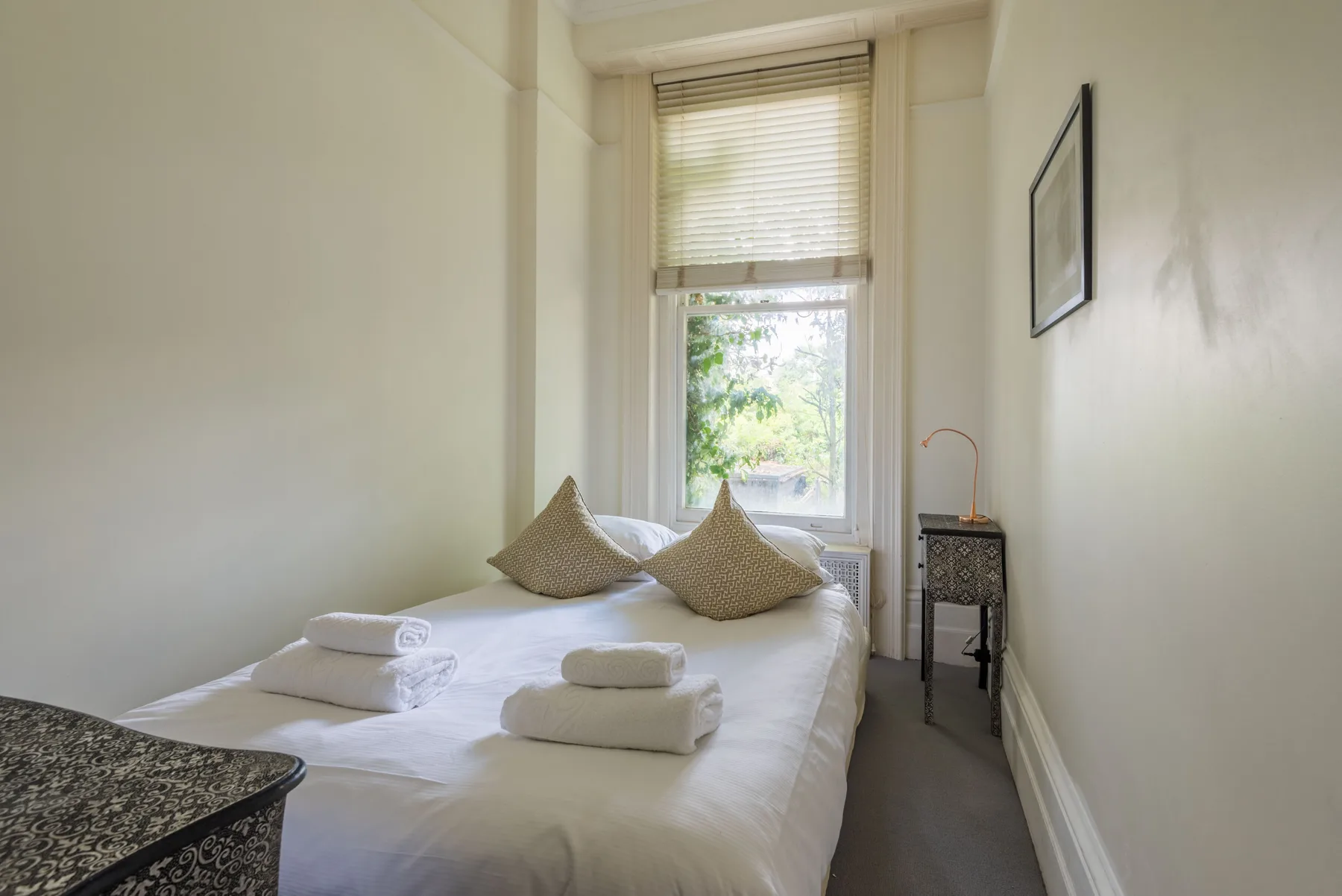 A bedroom with a bed beneath a window and a small bedside table.